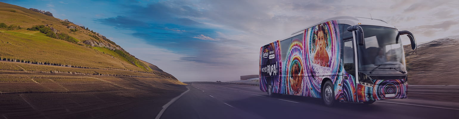 Autobus Suntago, ozdobiony grafiką z palmami. Na boku autobusu widoczny napis "Kup bilet na parkofpoland.com". W tle sylwetki palm i zachodzące słońce